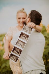 pregnancy photoshoot hugging husband holding up ultrasound pictures in a garden